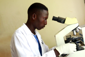 Vincent examines a sample under a microscope during his internship at Nagwere Health Centre III